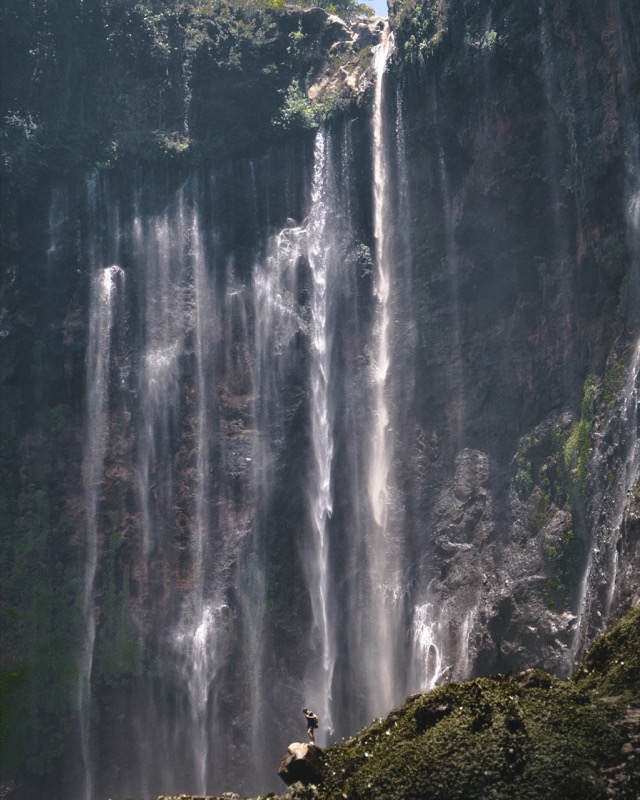tumpak sewu waterfall, java indonesia, man standing in front of huge waterfall